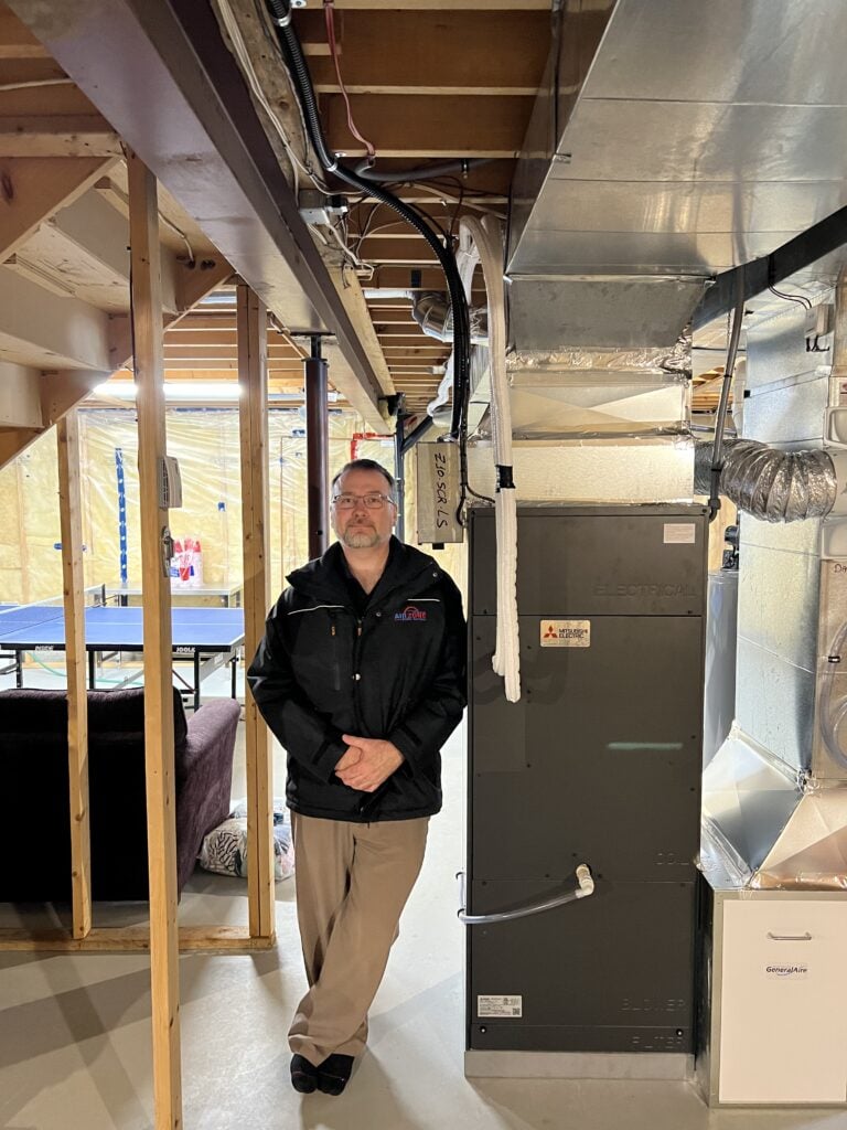 Matt standing beside a Mitsubishi ZUBA system installed in a home in Ottawa, Ontario by AirZone HVAC Services.